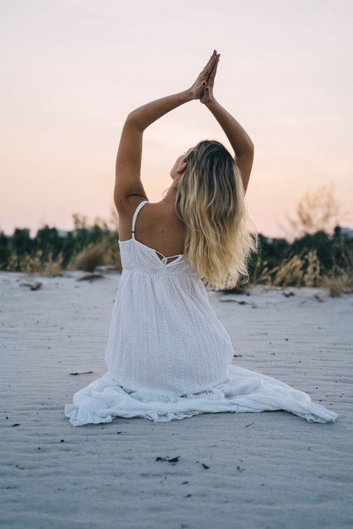 gallery-5 Woman in a white dress meditating on a serene beach during sunset, enhancing calmness and mindfulness.
